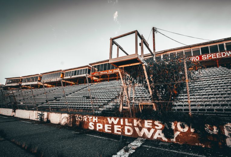 Abandoned North Wilkesboro Speedway with overgrown seating and a dilapidated viewing tower.